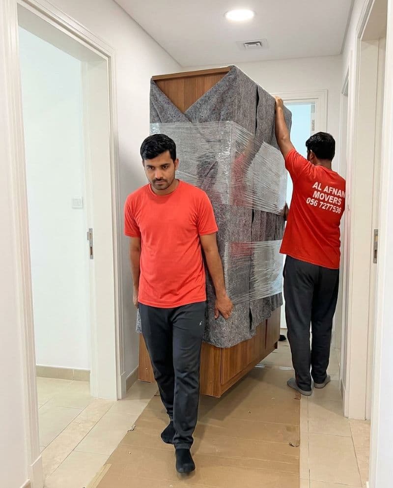 Al Afnan Furniture Transfer crew carrying a wrapped, padded wardrobe through a doorway