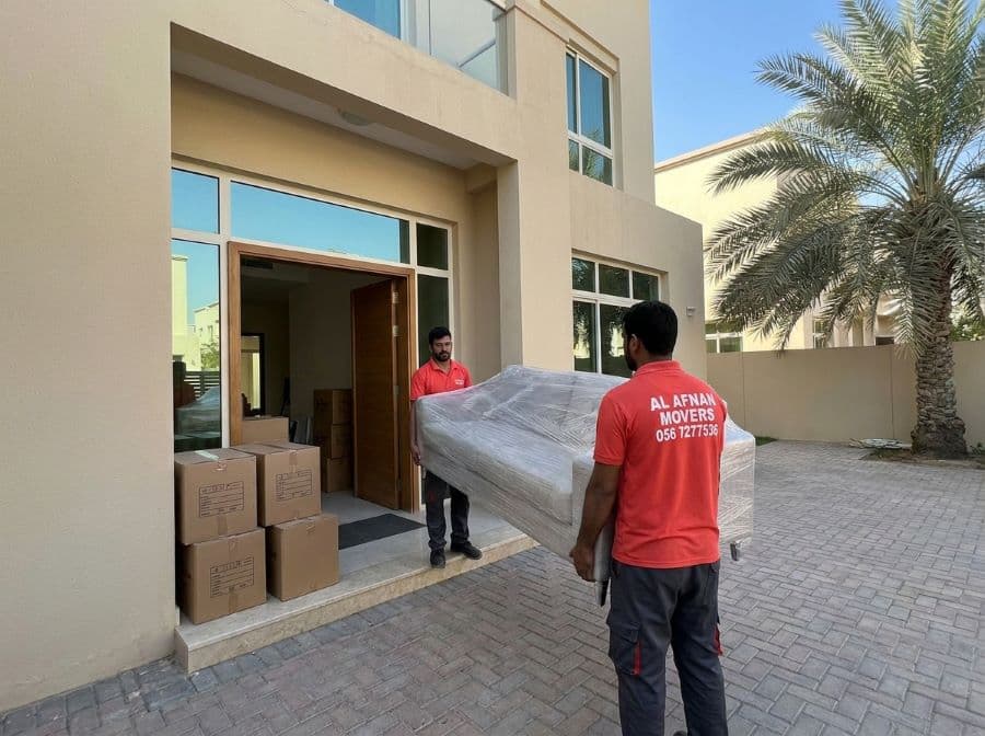 Al Afnan house movers carrying a stretch-wrapped sofa through a hallway with labelled boxes ready to load