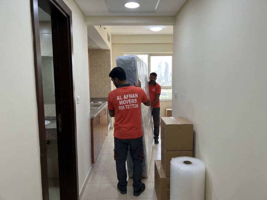 Studio movers in Ajman navigating narrow corridors and carefully angling furniture during a studio relocation