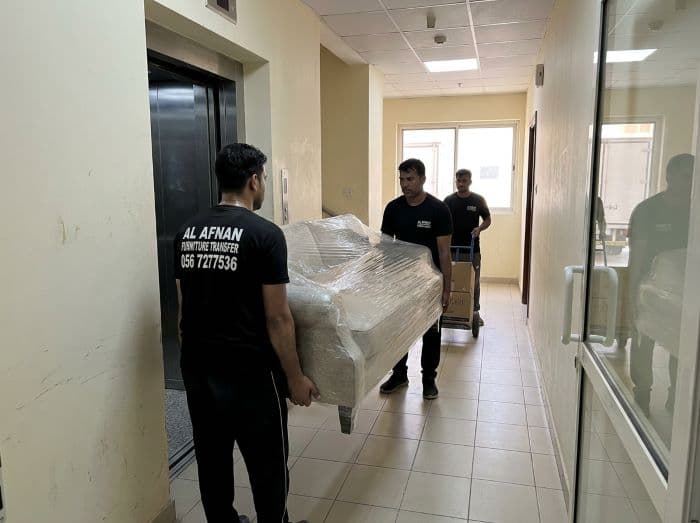 Apartment movers in Sharjah carefully moving wrapped furniture through a residential building corridor